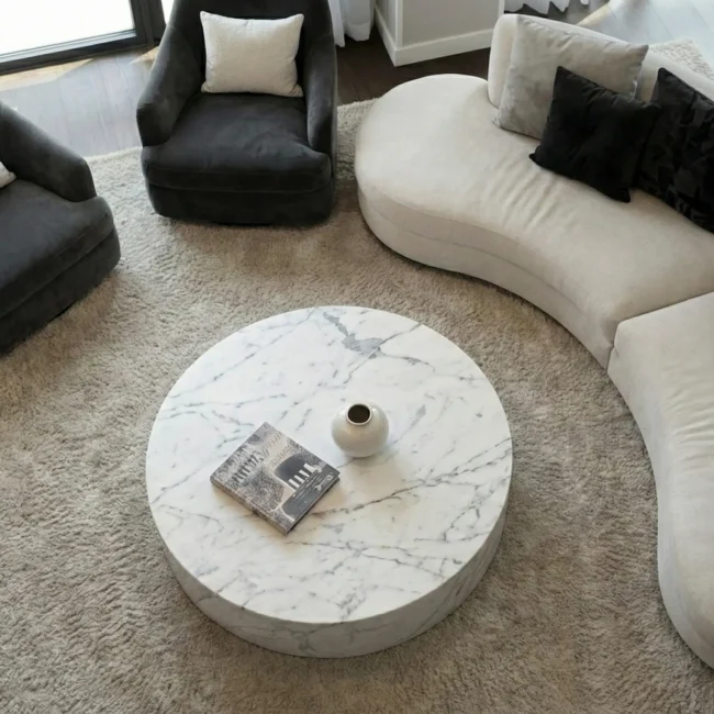 Top-down view of a luxury living room seating area featuring a round marble coffee table, curved cream sofa, and textured beige rug.