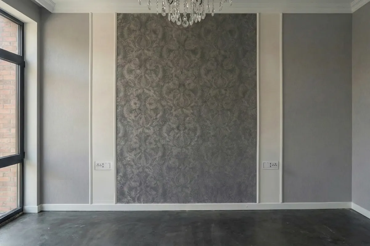 Empty modern bedroom during renovation featuring a grey damask wallpaper accent wall, white moldings, and a crystal chandelier.