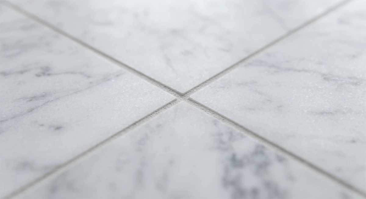 Macro close-up photograph capturing the flawless intersection point where four white marble tiles meet with perfect, clean grout lines, demonstrating high-quality installation craftsmanship