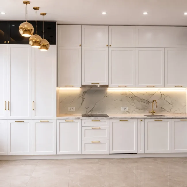 Completed modern luxury kitchen remodel featuring floor-to-ceiling white shaker cabinets, integrated appliances, a marble backsplash, and elegant gold pendant lights