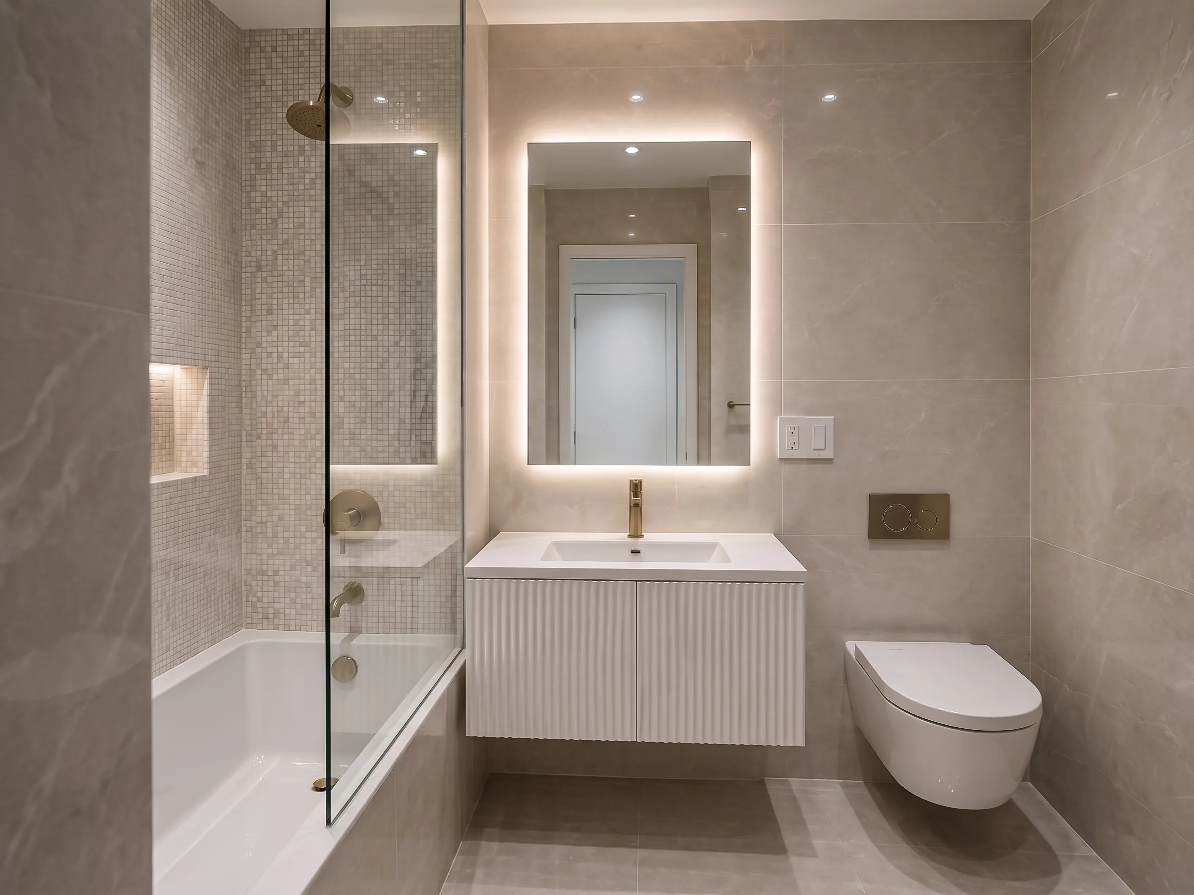 Completed modern bathroom remodel showcasing a floating white fluted vanity with a backlit LED mirror, a wall-mounted toilet, and a bathtub with a glass shower screen, matching the identical layout from the construction phase