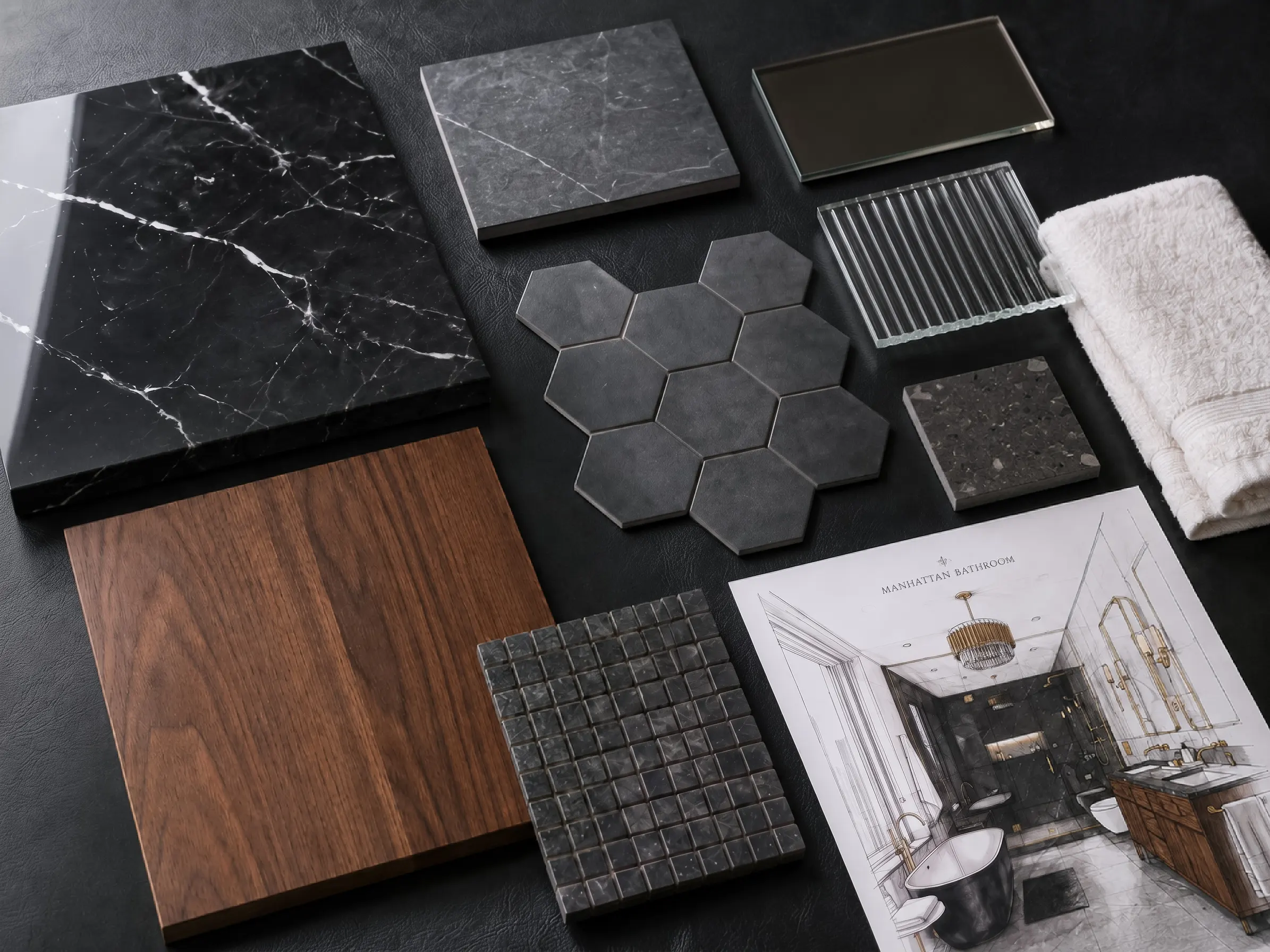 Flat lay material selection board for a high end bathroom remodel displaying black marble tiles, a walnut wood panel, dark grey hexagonal and mosaic tiles, fluted glass samples, and a color sketch showing the final design layout