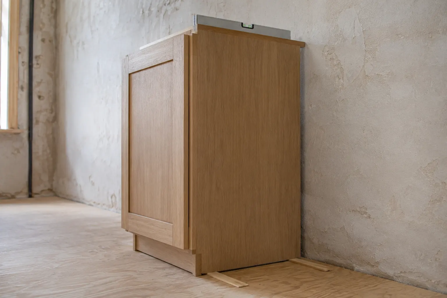 Wooden shims under a kitchen base cabinet with a spirit level resting on top