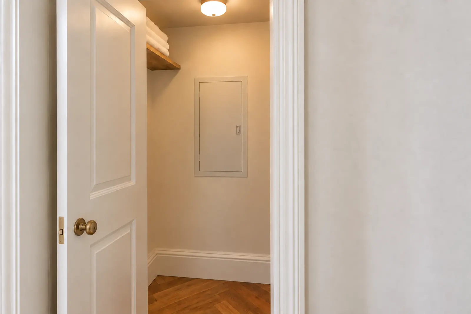 Hallway closet in a pre-war Manhattan apartment with a closed electrical panel set into the back wall