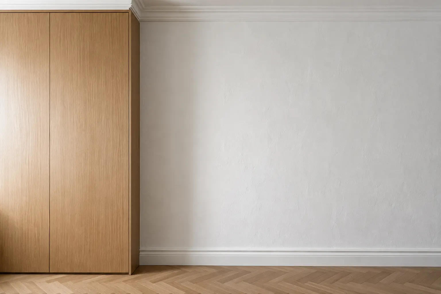 Tall flat-front white oak cabinet meeting an old plastered wall in a pre-war apartment, the vertical joint scribed tight, with plaster crown molding above, painted baseboard running up to the cabinet and a herringbone oak floor