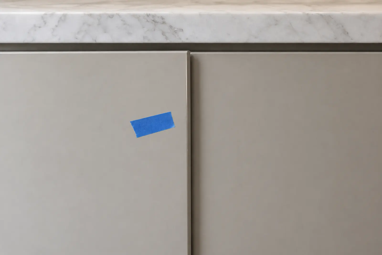 Two closed cabinet doors under a marble countertop, the left one standing slightly proud of the right and marked with blue painter's tape